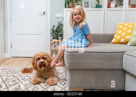 Flauschiger Hund Labradoodle oder Goldendoodle Hund, der sich mit einem Kind auf der Couch zu Hause mit einer natürlichen, modernen Einrichtung entspannt Stockfoto