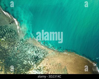Aus der Vogelperspektive auf eine pulsierende Küste mit türkisfarbenem Wasser, das auf eine strukturierte Küste trifft. Lombok, Gerupuk, Indonesien Stockfoto