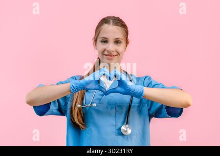 Junge kaukasische Ärztin in blauer Uniform auf einem isolierten rosa Hintergrund zeigt ein Herz mit Handschuhen, einen Ort für Text Stockfoto