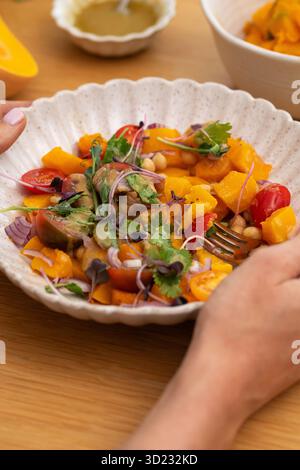 Person, die einen Teller mit herbstlich warmen Kichererbsen und gebratenem Kürbissalat mit frischen Kirschtomaten hält Stockfoto