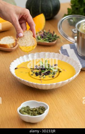 Brot von Hand in Gemüsesuppe mit Mikrogrün und Kürbis auf dem Tisch tauchen Stockfoto
