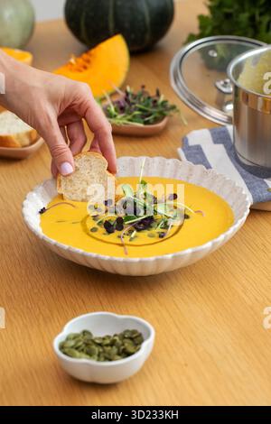 Brot von Hand in Gemüsesuppe mit Mikrogrün und Kürbis auf dem Tisch tauchen Stockfoto