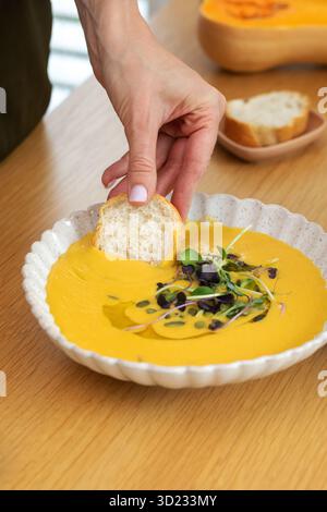 Brot von Hand in Gemüsesuppe mit Mikrogrün und Kürbis auf dem Tisch tauchen Stockfoto