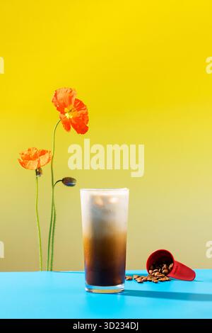 Erfrischender Eiskaffee mit Sahne in einem hohen Glas, umgeben von lebendigen Mohnblumen Stockfoto