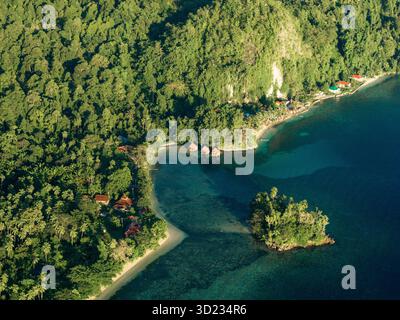 Blick aus der Vogelperspektive auf die üppige grüne tropische Küste mit ruhigem blauem Wasser und einem kleinen Küstendorf. Saleman Village, Seram Island, Indonesien Stockfoto