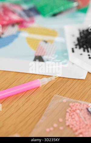 Eine Nahaufnahme einer Hand, die Kristalle auf einer Leinwand für ein Diamantmalprojekt platziert. Diamantmosaik Stockfoto