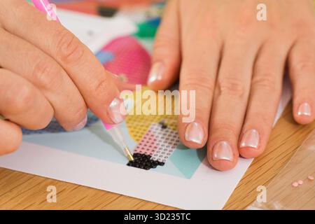Eine Nahaufnahme einer Hand, die Kristalle auf einer Leinwand für ein Diamantmalprojekt platziert. Diamantmosaik Stockfoto