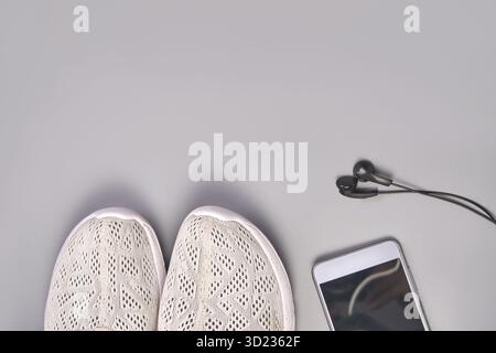 Weiße Sneakers mit Smartphone und Ohrstöpseln auf grauer Oberfläche Stockfoto