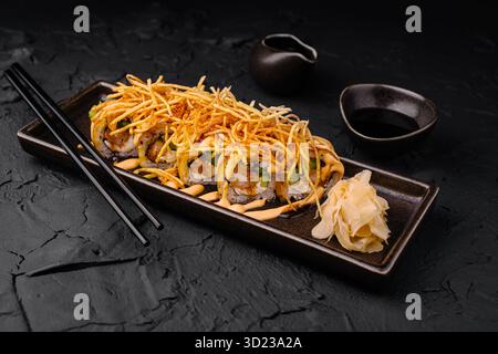Sushi-Brötchen garniert mit knusprigen Belägen auf einem dunklen Teller serviert Stockfoto