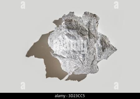 Silberne Aluminiumfolie zerknittert zu einer Kugel mit Schatten auf neutralem Hintergrund Stockfoto