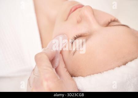 Junge weiße Frau genießt eine entspannende Gesichtsmassage mit Rosenquarz Gua Stockfoto