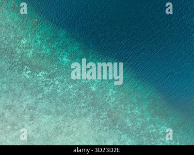Aus der Vogelperspektive auf ein tiefblaues Meer, das auf einen leichten Sandboden entlang einer diagonalen Linie trifft. Pantai Ngurbloat oder Ngurbloat Beach in Kei Kecil im Südosten von Maluku, Indonesien Stockfoto