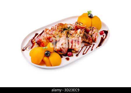 Gourmet-Gericht mit gerolltem Fleisch und Obst, serviert auf einem weißen Teller Stockfoto