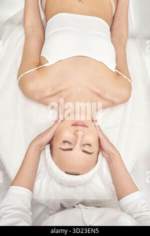 Junge kaukasische Frau, die entspannende Gesichtsmassage in Spa-Umgebung erhält Stockfoto