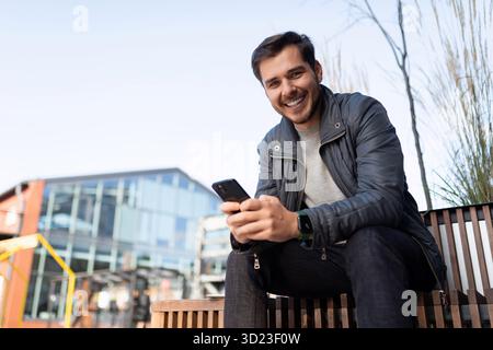 Junger Mann in Jacke mit Telefon draußen Stockfoto