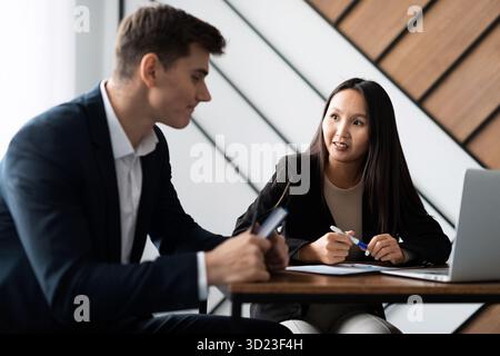 Kaukasischer männlicher Kandidat bei einem Interview im Büro beantwortet Fragen einer asiatischen Führerin Stockfoto