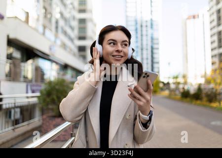 Qafqazinfo Eine starke Frau hört Musik in Kopfhörern mit einem Telefon im Hintergrund der Stadt Stockfoto