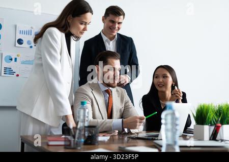Lächelnd treffen sich verschiedene Kollegen in einem Brainstorming in der Vorstandsetage, um gemeinsam Finanzstatistiken zu diskutieren Stockfoto