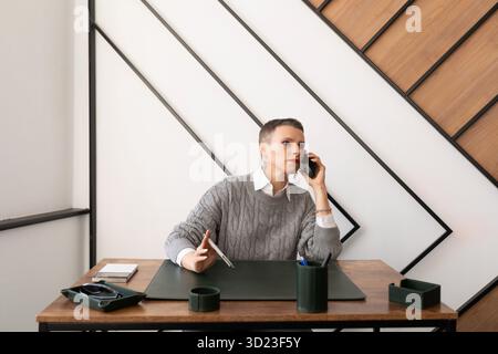 Eine Geschäftskaukasierin, eine ernsthafte Frau, die mit dem Handy telefoniert, während sie im Büro am Tisch sitzt Stockfoto