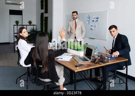 Ein Team von Geschäftsleuten, die auf einem großen Desktop mit Laptops und Dokumenten über das Geschäft diskutieren Stockfoto