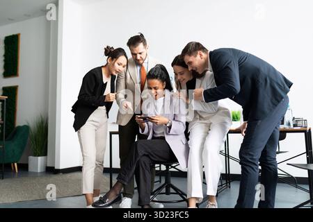 Mitarbeiter im Büro stehen um eine Frau, die auf einem Smartphone spielt Stockfoto