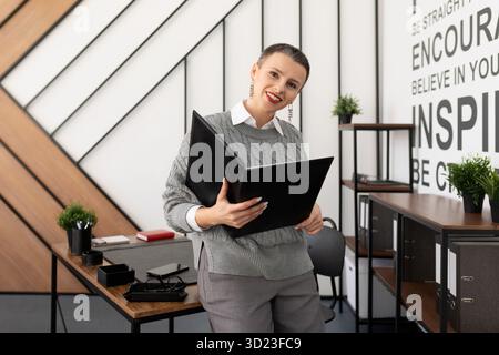 Eine lächelnde Geschäftsfrau, die in die Kamera schaut, mit einem Ordner für Papiere und Dokumente in ihren Händen Stockfoto