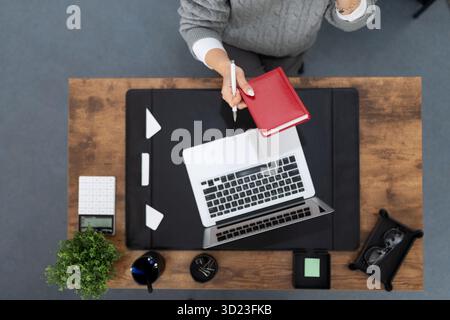 Geschäftsfrau, die an einem Laptop arbeitet und ein Notebook in der Hand hat, Desktop-Ansicht von oben Stockfoto