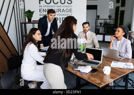 Mitarbeiter des Unternehmens diskutieren während einer Besprechung im Büro auf einem großen Desktop mit Laptops und Dokumenten Stockfoto