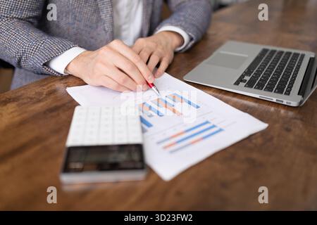 Ein Geschäftsmann folgt einer Verkaufstabelle in Form von Spalten auf einem Tisch neben einem Laptop und einem Taschenrechner Stockfoto