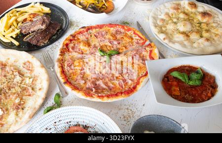 Auf dem Tisch gibt es verschiedene köstliche italienische Gerichte, die eine reichhaltige und einladende Mahlzeit schaffen Stockfoto