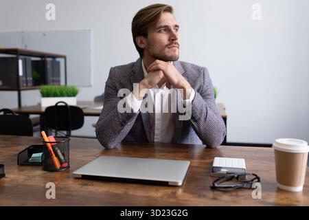 Reifer seriöser Geschäftsmann sitzt am Tisch und blickt nachdenklich aus dem Fenster Stockfoto