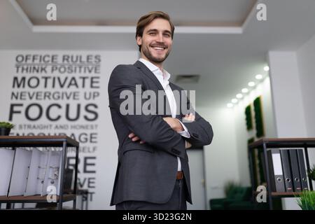 Ein erfolgreicher Geschäftsmann in einem Business-Anzug steht im Büro und sieht sich eine Superkamera an Stockfoto
