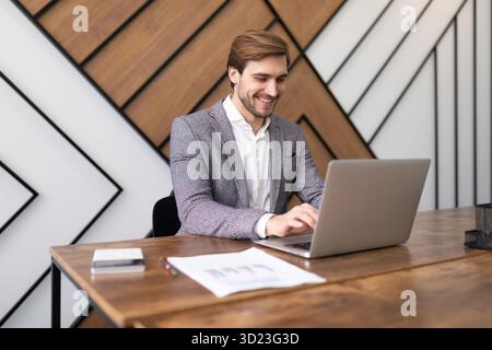 Ziemlich erfolgreicher Geschäftsmann, der im Büro an einem Laptop arbeitet Stockfoto
