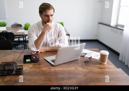 Müder Geschäftsmann, der die Steuererklärung auf dem Laptop in einem eleganten Büro ausfüllt Stockfoto