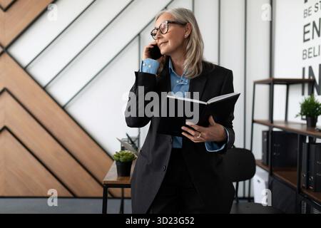 50-jährige Rechtsanwältin, die im Büro auf einem Mobiltelefon spricht. Steuerbuchhalter Consultant Frau, die Buchhaltung von Konten Stockfoto