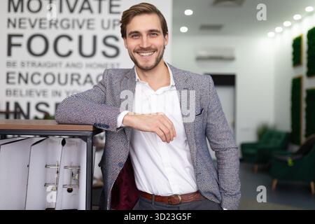 Liebenswerter junger Geschäftsmann in einem Business-Anzug mit einem Lächeln mitten im Büro Stockfoto
