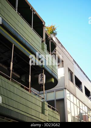 Grün gekachelte Gebäudefassade in der Nähe des Bahnhofs Kichijoji mit einer hängenden japanischen Laterne und moderner gemischter Architektur unter klarem blauem Himmel Stockfoto