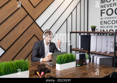 Geschäftsmann im Büro auf einem Laptop mit Kopfhörern, der ein Webinar ansieht Stockfoto