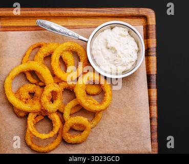 Knusprige Zwiebelringe serviert mit cremigem Dip auf Holzplatte Stockfoto