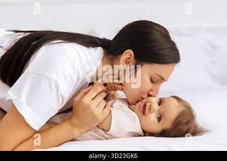 Liebevolle Mutter liegend auf dem Bett und küsste liebevoll ihre Babywange Stockfoto