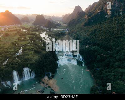 Blick aus der Vogelperspektive auf atemberaubende Wasserfälle, die bei Sonnenuntergang durch die üppigen grünen Berge kaskadieren. Ban Gioc Waterfalls, TR˘ng KH·nh District, Cao Bang, Vietnam Stockfoto