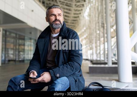 Erwachsener bärtiger Geschäftsmann, der auf das Einsteigen in ein Flugzeug im Flughafengebäude wartet. Stockfoto