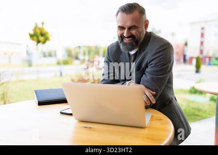 Reifer Geschäftsmann, der am Laptop arbeitet und draußen lächelt Stockfoto