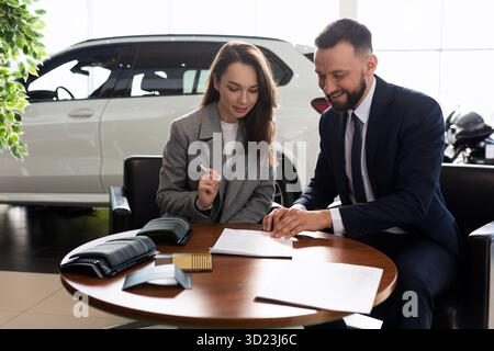 Eine junge Frau kauft ihr erstes Auto in einem Autohändler und unterzeichnet einen Versicherungsvertrag Stockfoto