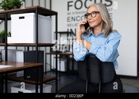 Erwachsene starke unabhängige Anwältin, die auf dem Handy spricht, während sie im Büro auf dem Stuhl sitzt. Professionelle Buchprüferin Stockfoto