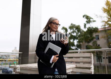 Erfolgreiche weiße Frau mit Laptop und Telefon eilt zu einem Meeting Stockfoto