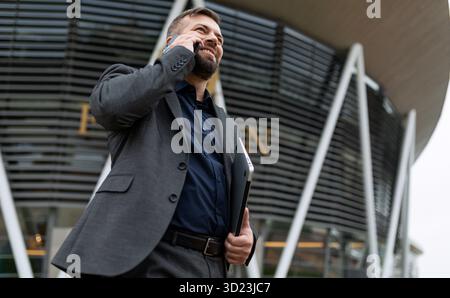 Erfolgreicher erwachsener Geschäftsmann in einem Business-Anzug mit einem Lächeln im Gesicht zufrieden mit dem Gespräch auf einem Mobiltelefon Stockfoto