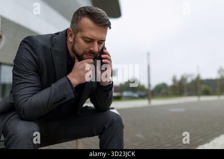 Nahaufnahme eines Geschäftsmannes mit einem Telefon in der Hand, während er mit einem nachdenklichen Ausdruck spricht Stockfoto