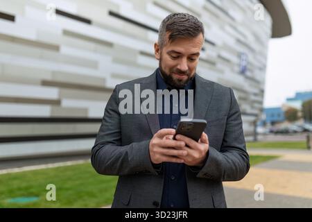 Ein erwachsener Geschäftsmann im klassischen Anzug schaut überrascht auf den Bildschirm des Telefons Stockfoto