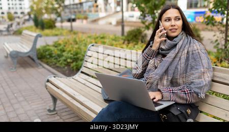 Freiberufliche Mitarbeiterin, die online auf einem Laptop arbeitet, während sie in der Stadt auf Holzbänken sitzt Stockfoto